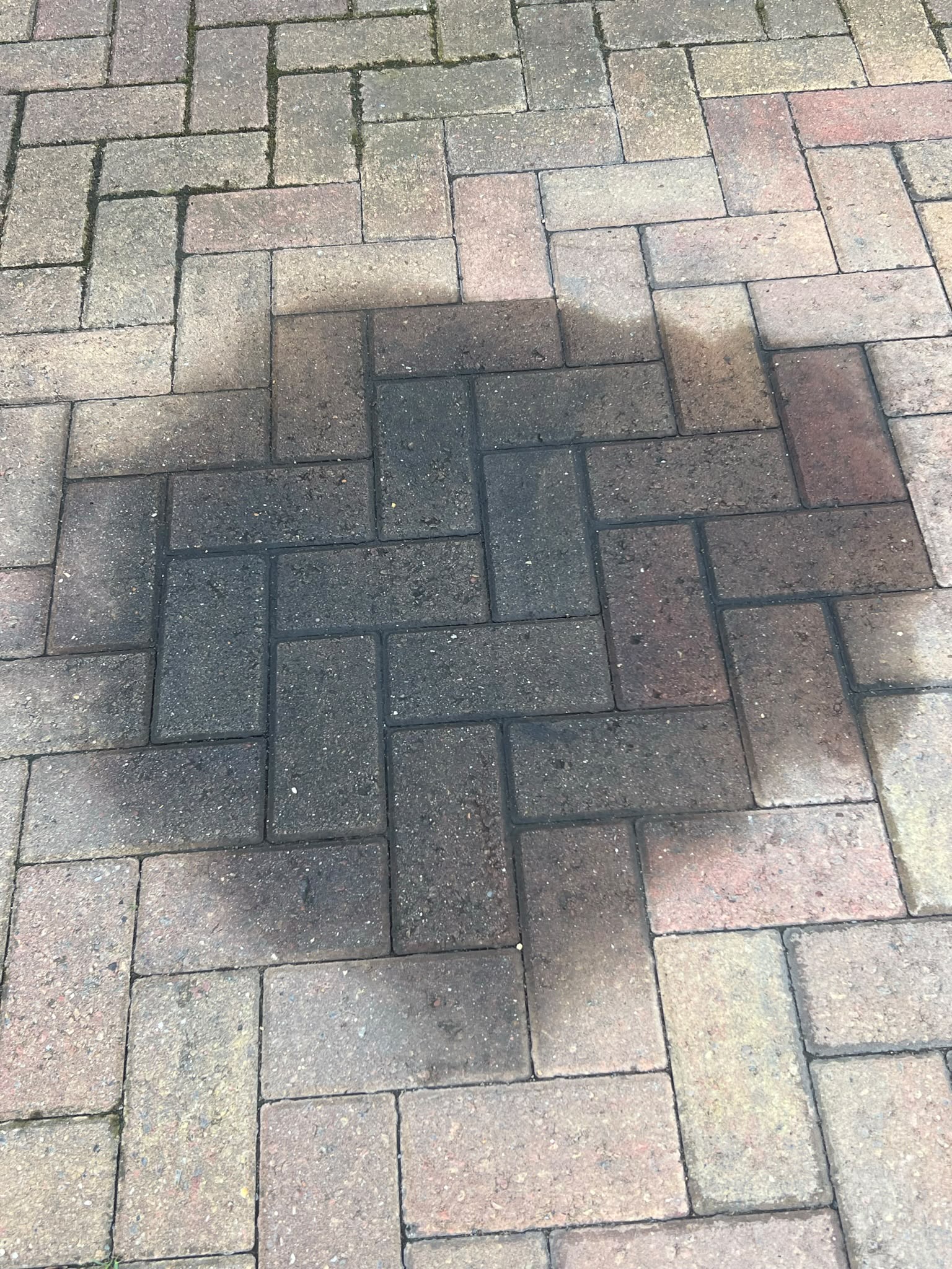 Close-up of herringbone block paving with a large dark circular stain covering several bricks