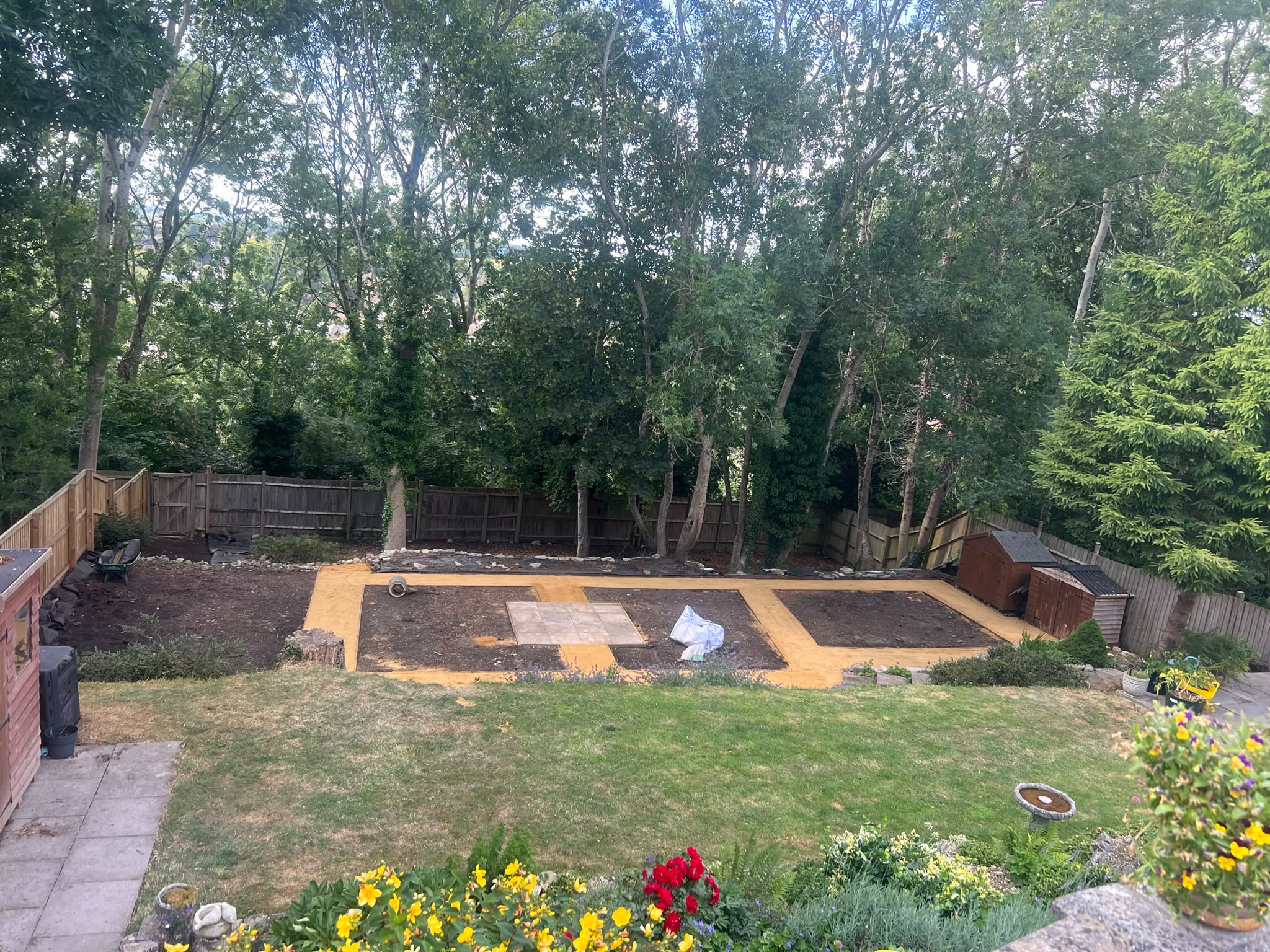 High-angle view of a garden under construction with sand paths framing soil beds, paving started, and materials on site