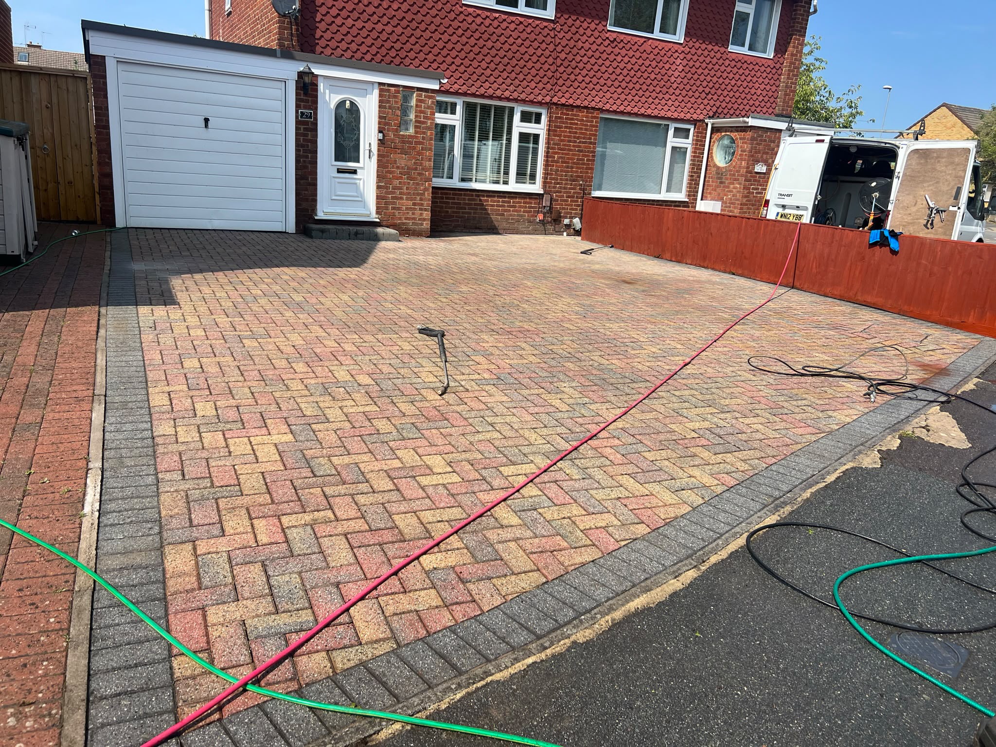 Herringbone block-paved driveway with pressure washer wand and red hose from an open white work van