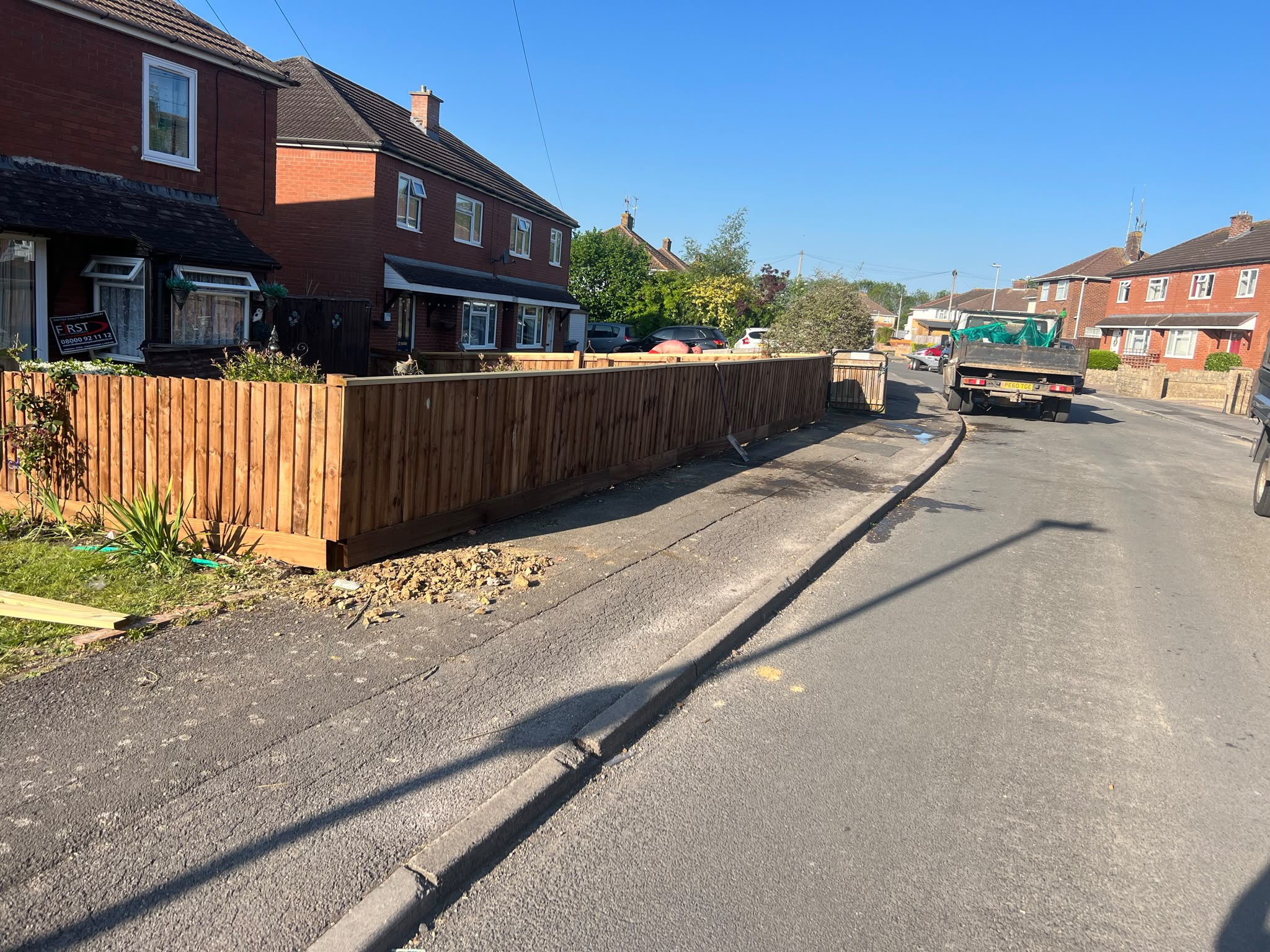 Fresh brown featheredge fence with top rail along a front garden on a sunny residential street