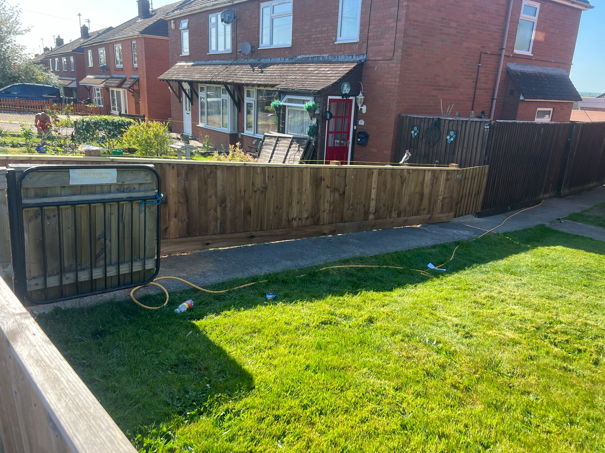 New light timber closeboard fence with yellow leveling string along the top beside a green lawn and brick houses