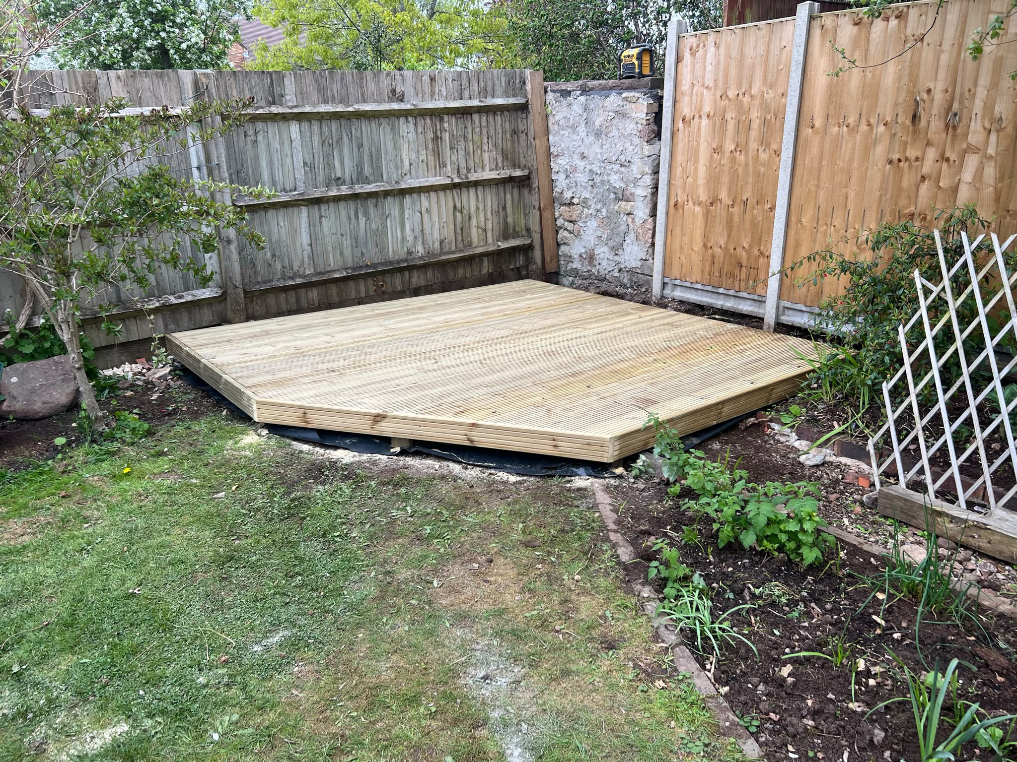 Newly finished light timber deck with clipped corner set between wooden fences over weed membrane