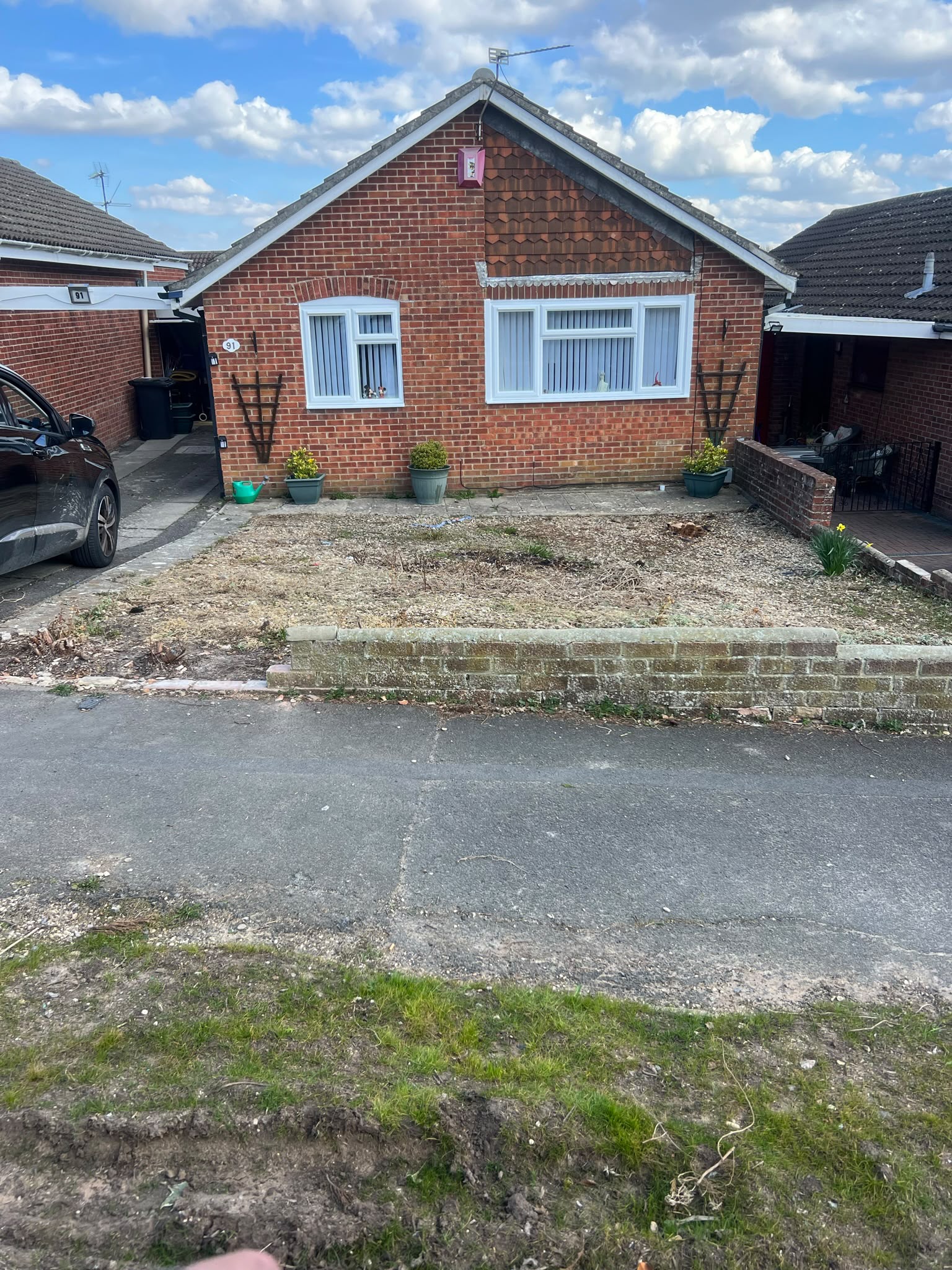 Cleared front garden bed of bare soil and woodchip with a stump beside a red brick bungalow