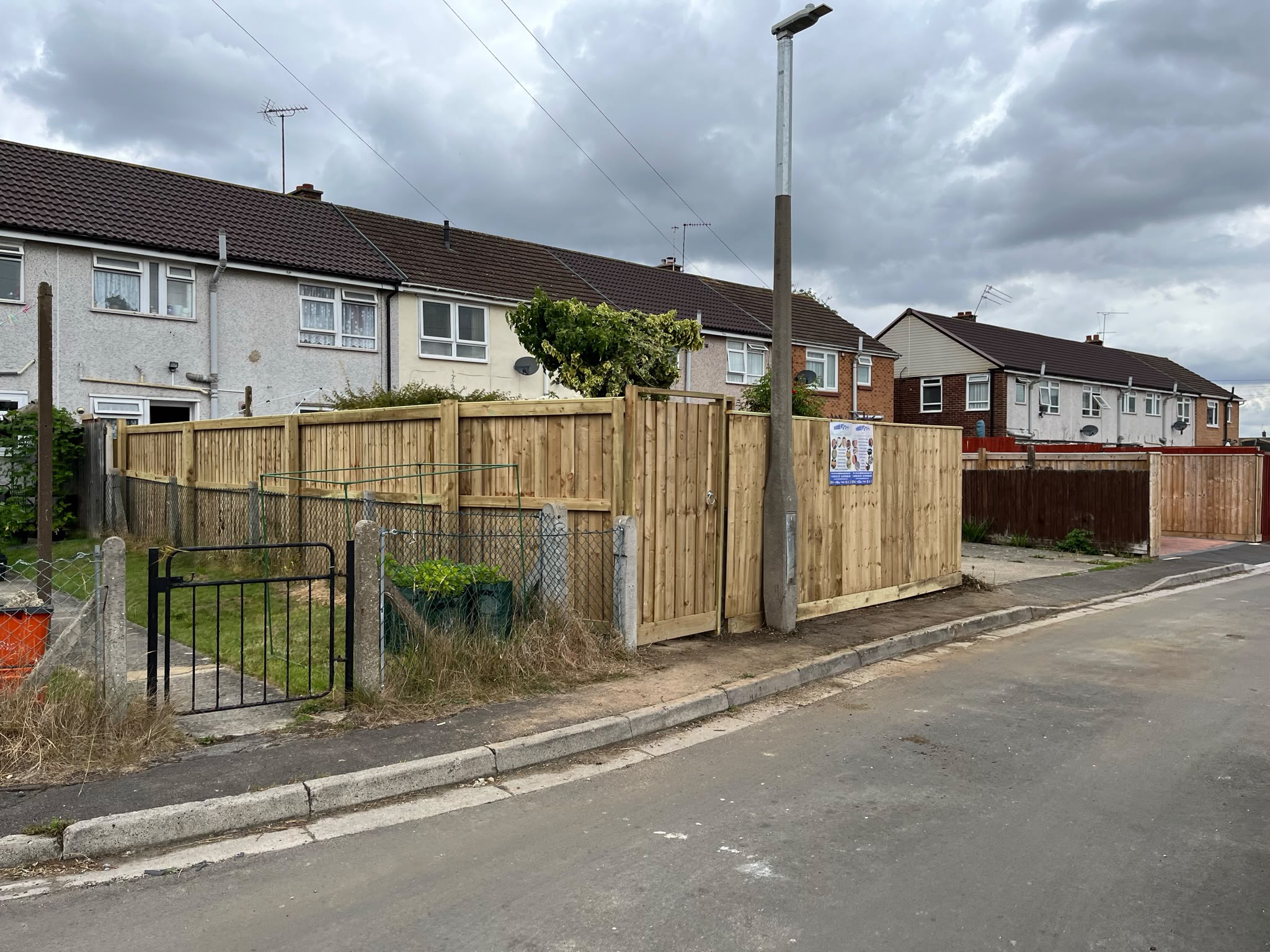 New light closeboard fence and matching gate along a residential street corner with houses behind