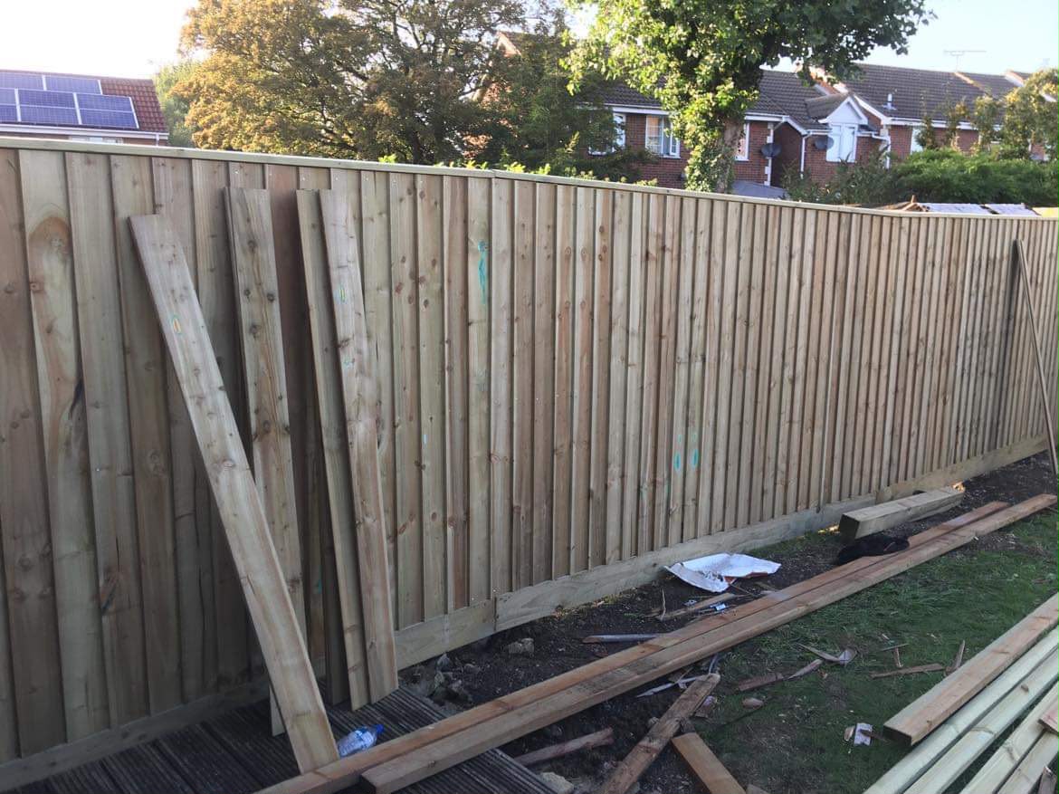 Long new featheredge fence with capping rail, spare boards leaning against it and offcuts on the soil