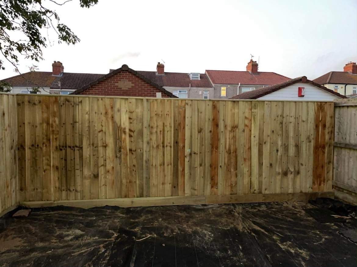 Tall new featheredge timber fence with gravel board over black weed membrane and rooftops beyond