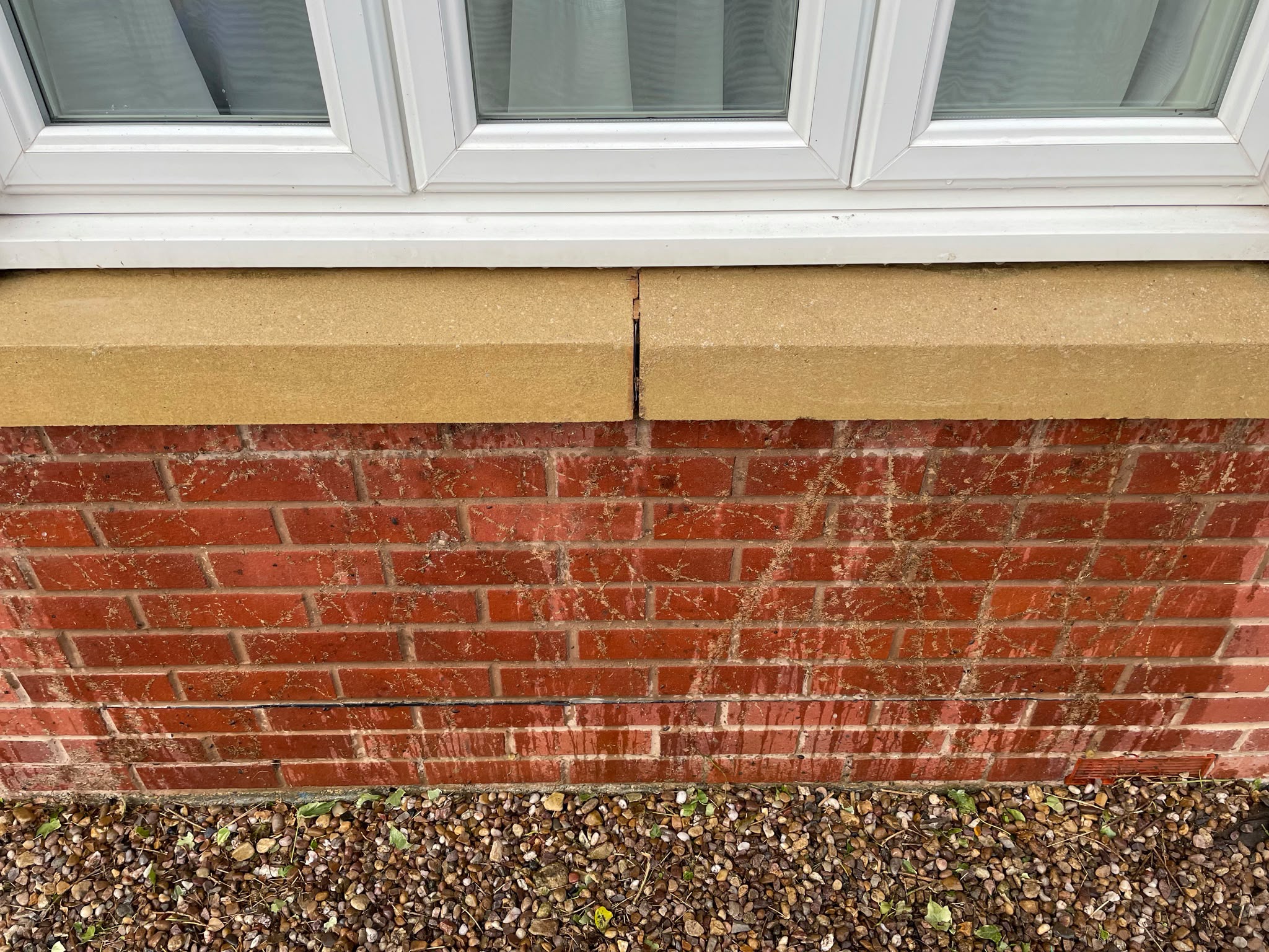 Red brick wall under a window showing dried sucker marks and stains after climbing plant removal above gravel